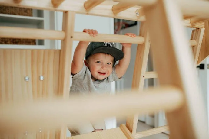 toddler hanging on natural wooden play set